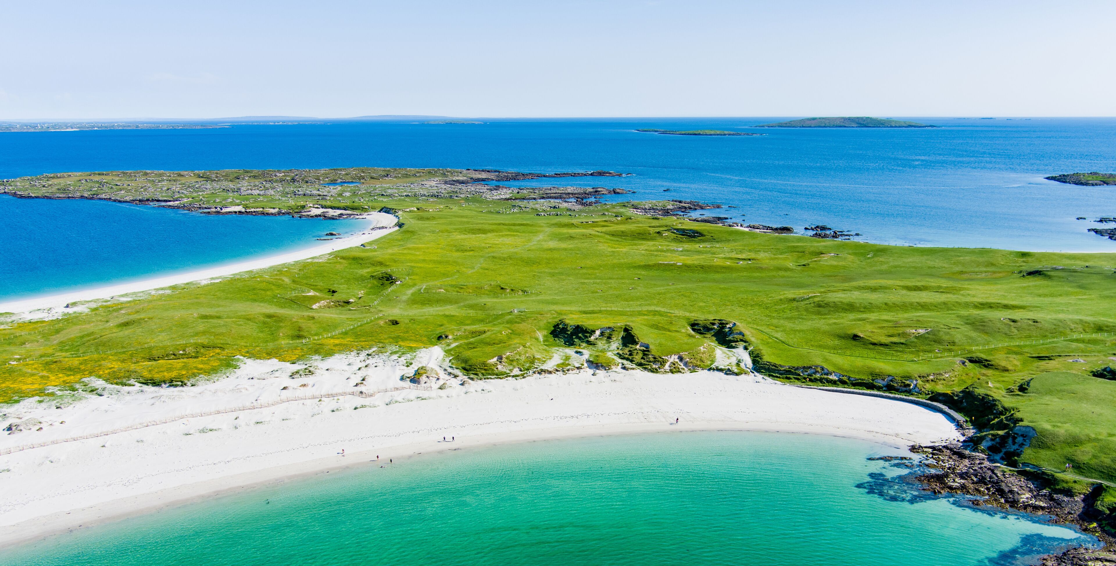 A coastal landscape with a sandy beach, a grassy area, and a clear blue sea.
