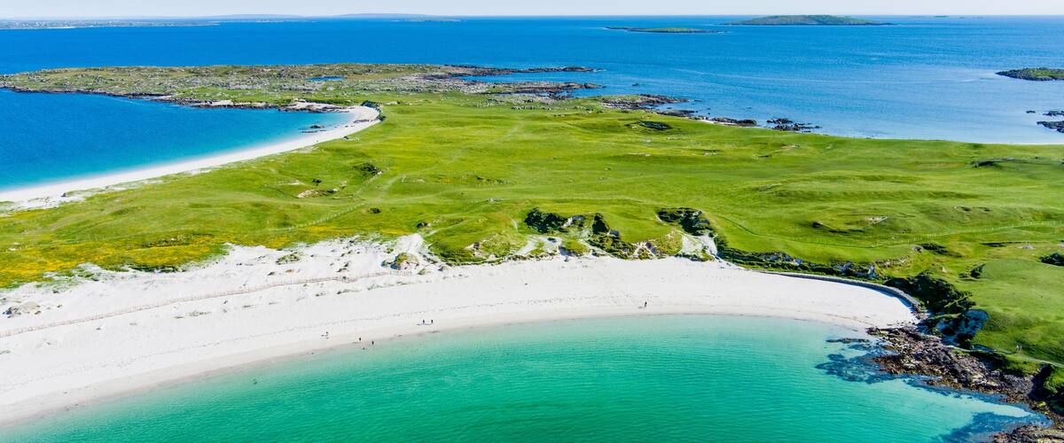 A coastal landscape with a sandy beach, a grassy area, and a clear blue sea.