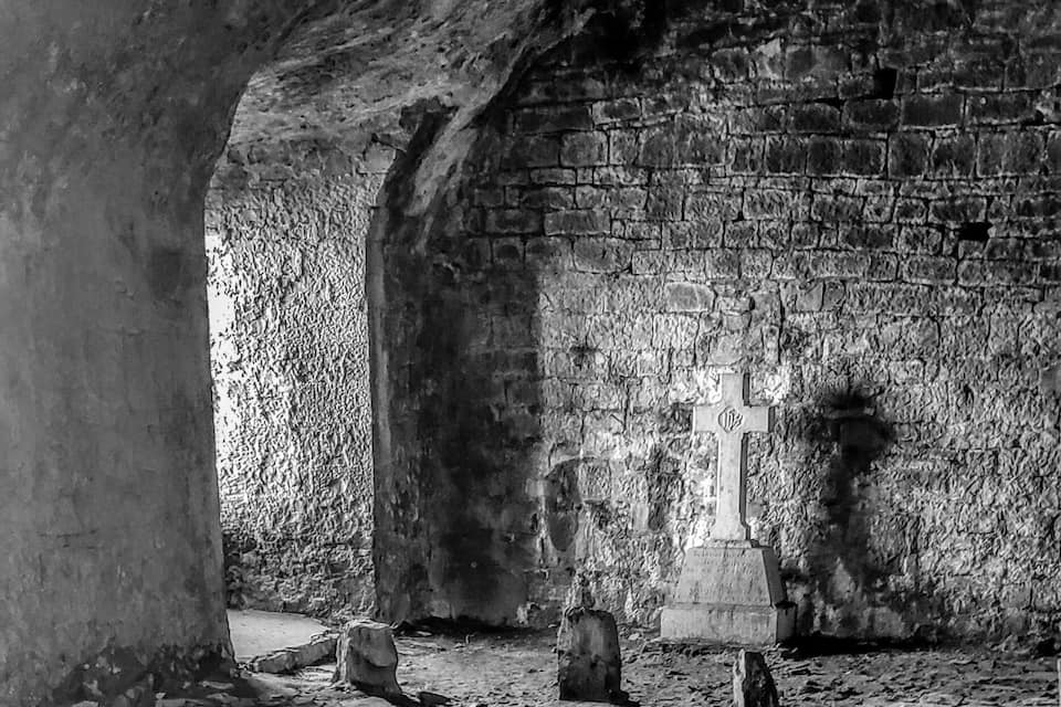 An ancient stone floor with scattered stones and a cross in the background.