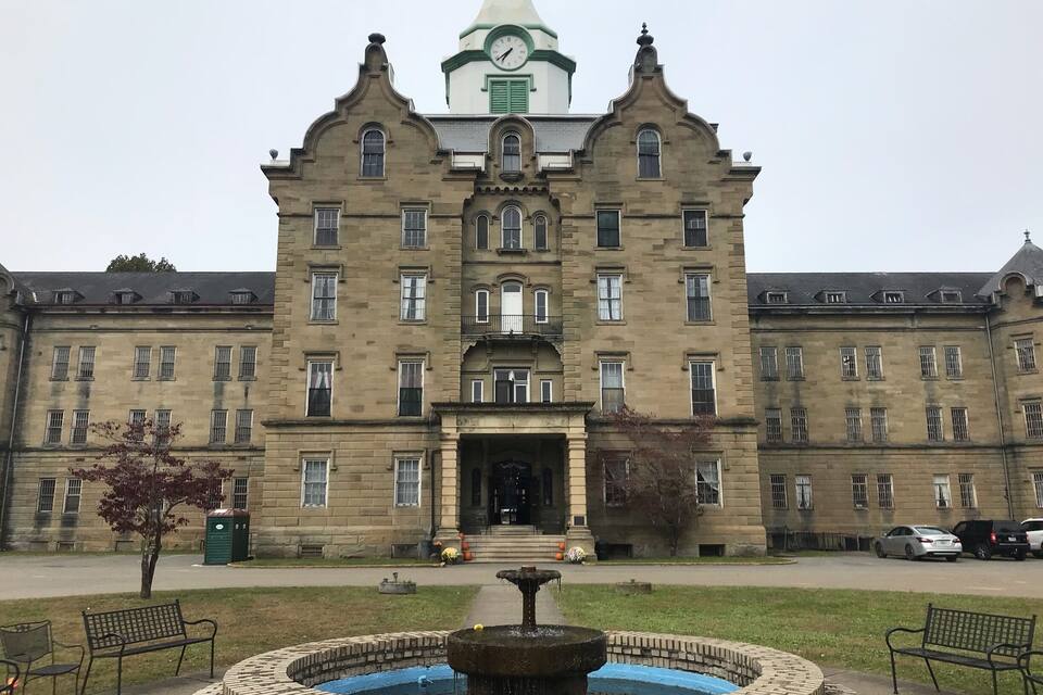 Un edificio grande e histórico con una torre de reloj y una fuente en la fachada.