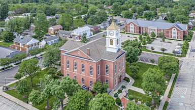 A large brick building with a clock tower, surrounded by trees and a parking lot.