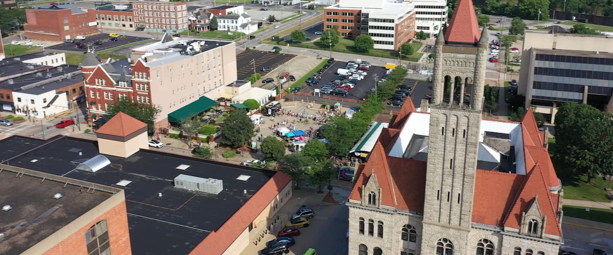 A town square with historic buildings, a church with a tall steeple, and a parking lot.