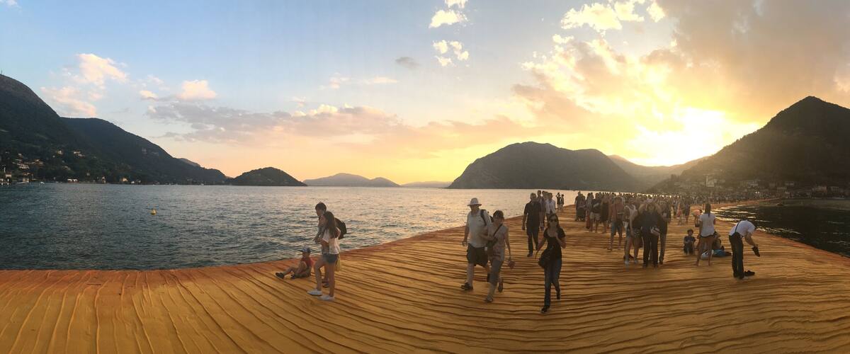 A wooden deck overlooking a lake with mountains in the background and a sunset.
