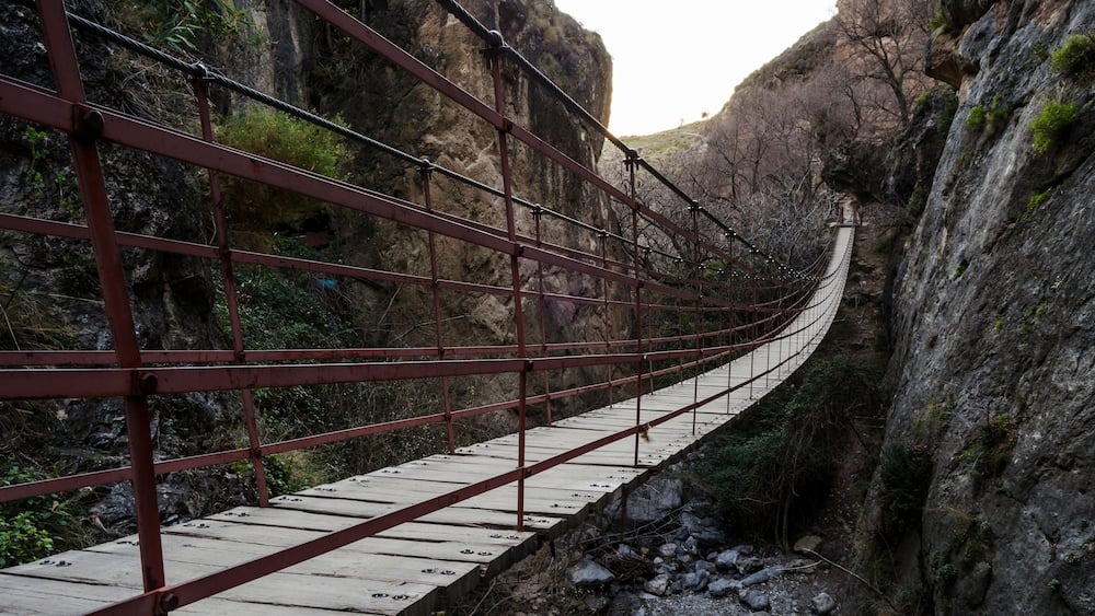Un pont suspendu dans un canyon rocheux, doté de garde-corps métalliques et de planches de bois.
