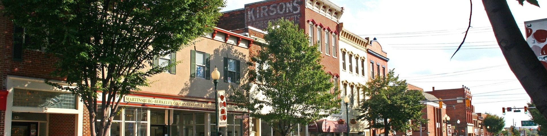 Una calle bordeada de edificios históricos, incluyendo un letrero que dice 'KIRSONS' y 'MARTINSBURG-BERKELEY CO. CONVENTION & VISITORS'.