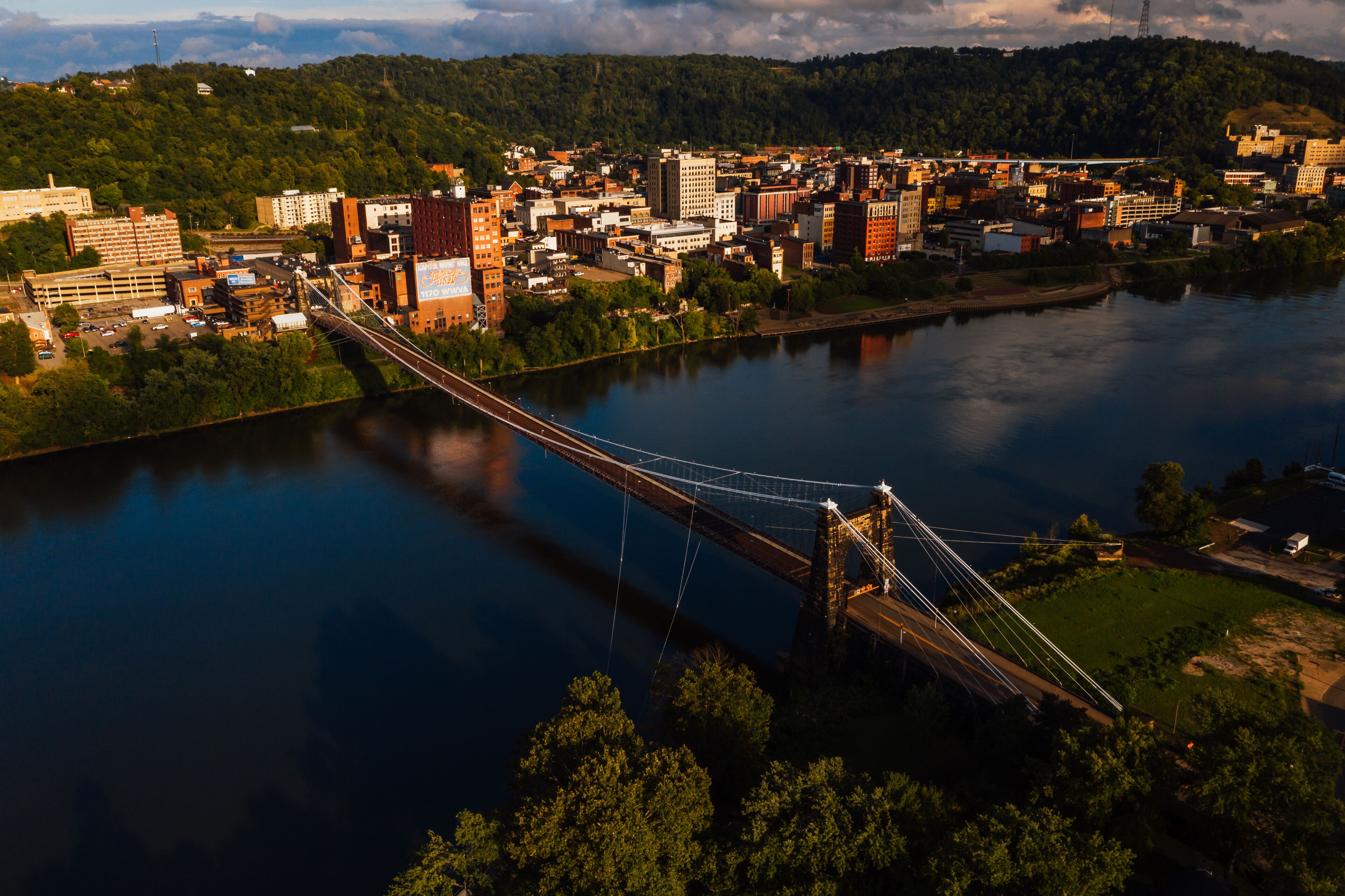 This is an aerial view of the historic Wheeling Suspension Bridge that carries the National Road over the still blue waters of the Ohio River in Wheeling, West Virginia.