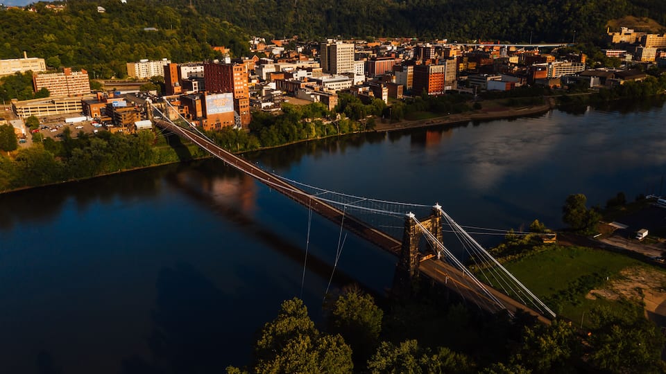 A suspension bridge over a river, surrounded by a cityscape with buildings and greenery.