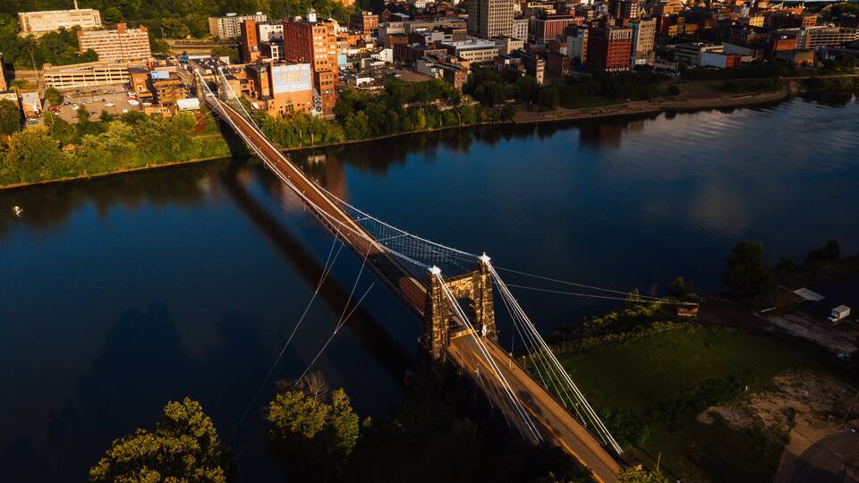A suspension bridge over a river with a cityscape in the background.