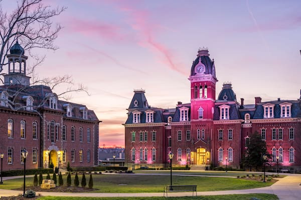 A historic building with a clock tower and a dome, surrounded by a well-maintained lawn and street lamps.
