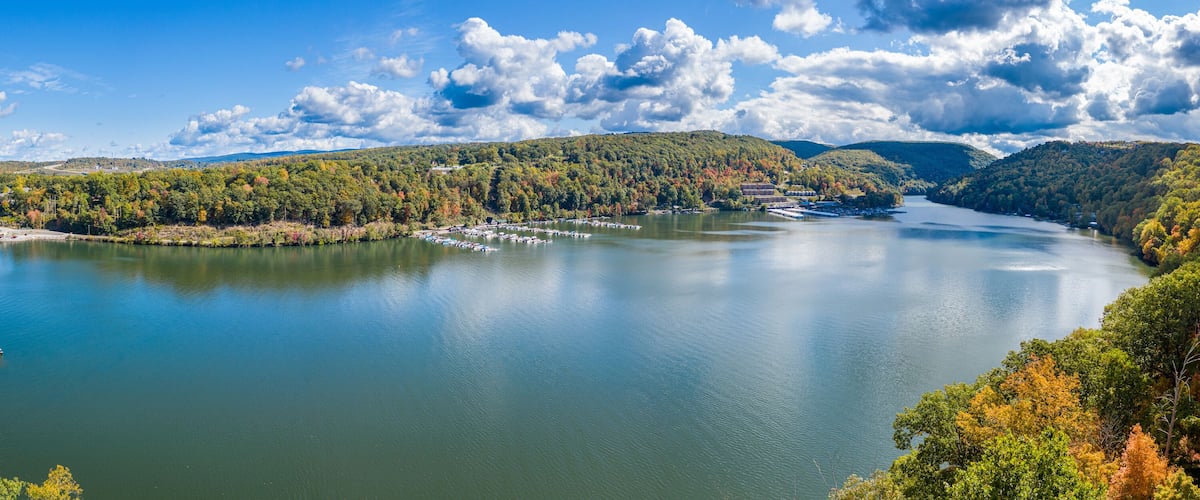 A lake with a bridge, surrounded by hills and autumn-colored trees.