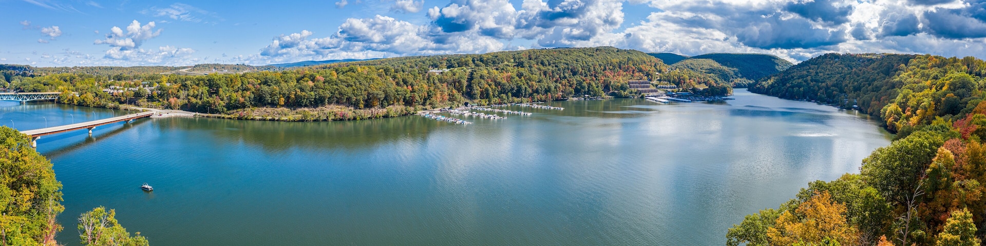 A lake with a bridge, surrounded by hills and autumn-colored trees.