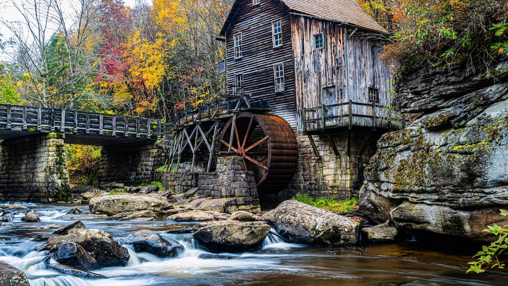 A wooden mill with a water wheel, a stone bridge, and a river.
