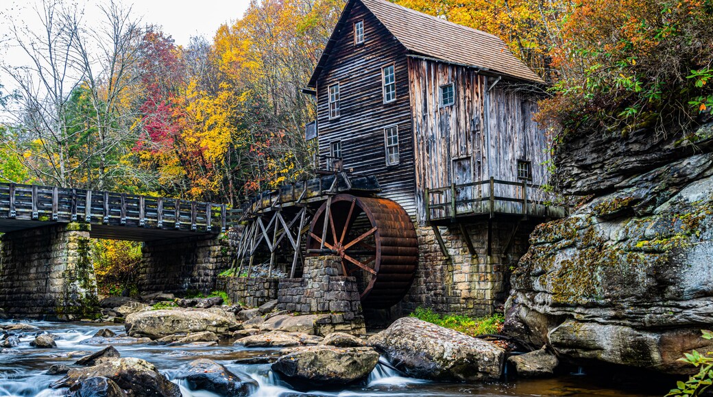 A wooden mill with a water wheel, a stone bridge, and a river.
