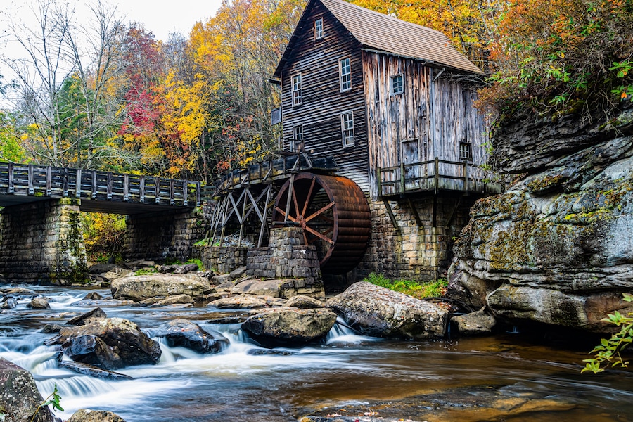 A wooden mill with a water wheel, a stone bridge, and a river.