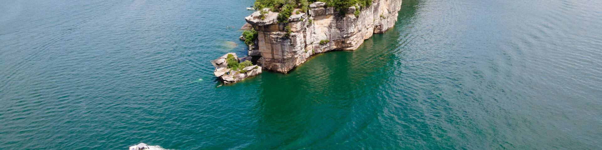 A large island surrounded by a calm lake, with a boat creating a wake.