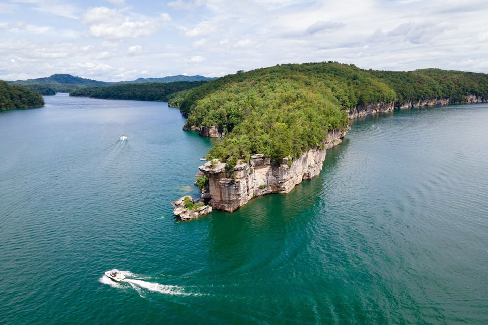 A large island surrounded by a calm lake, with a boat creating a wake.