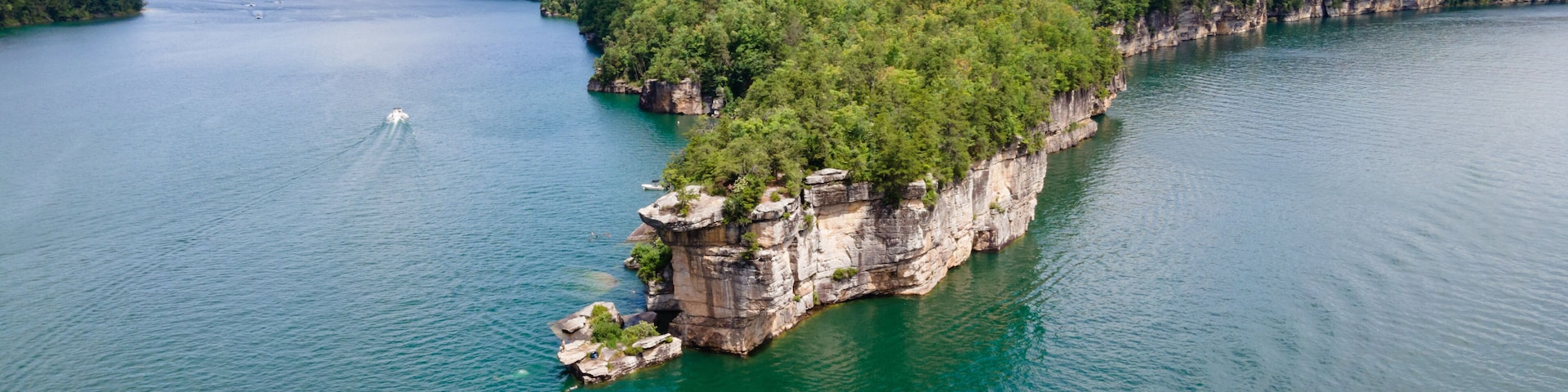 A large island surrounded by a calm lake, with a boat creating a wake.