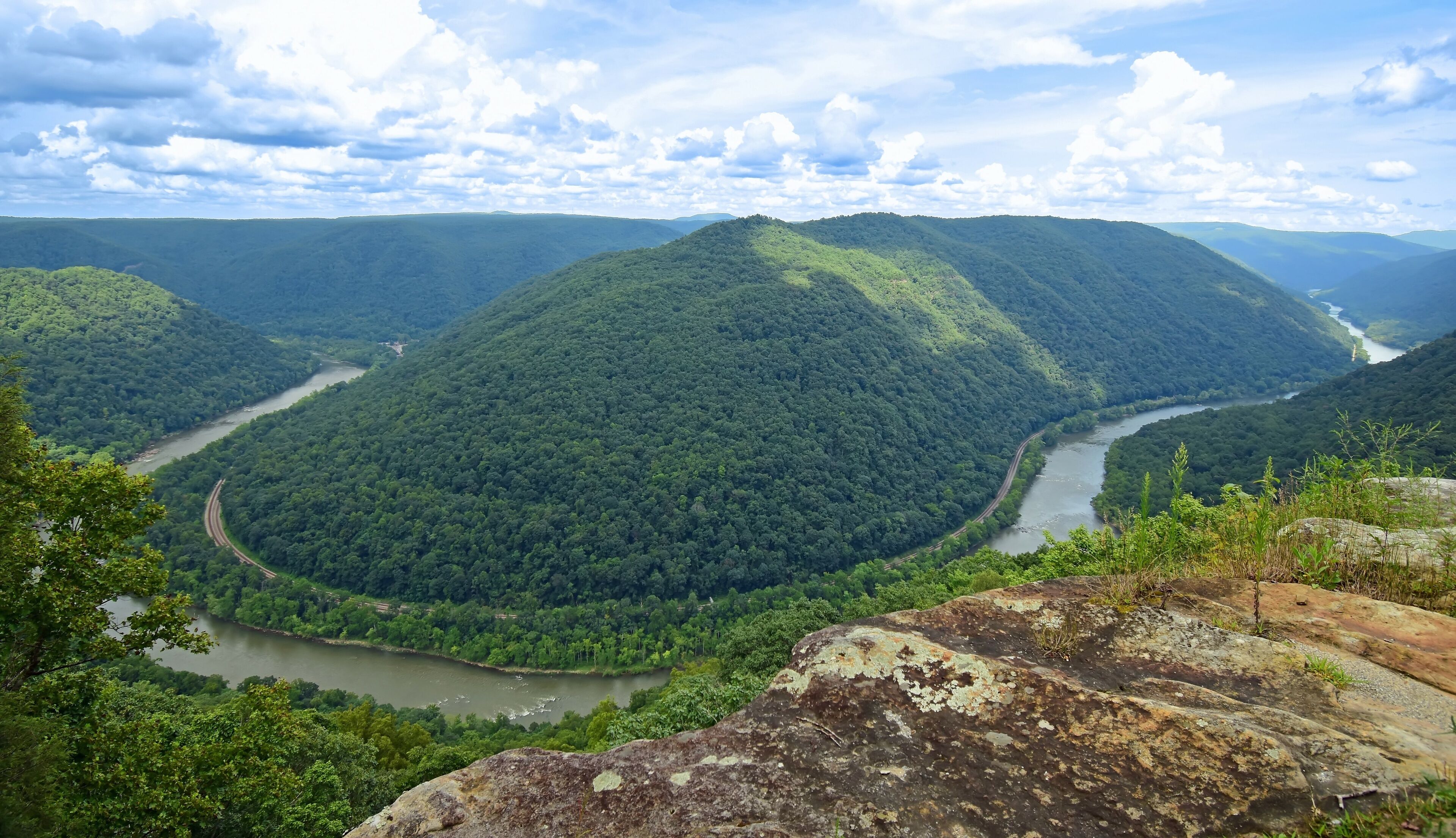 looking out at a horseshoe bend in the new river, railway,   and forested  hills in summer from the grandview main overlook in the new river gorge national park, west virginia