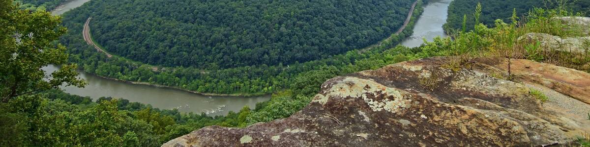 looking out at a horseshoe bend in the new river, railway, and forested hills in summer from the grandview main overlook in the new river gorge national park, west virginia
