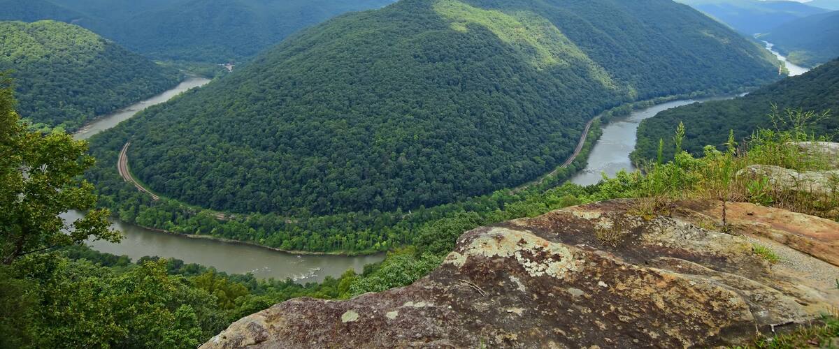 looking out at a horseshoe bend in the new river, railway, and forested hills in summer from the grandview main overlook in the new river gorge national park, west virginia