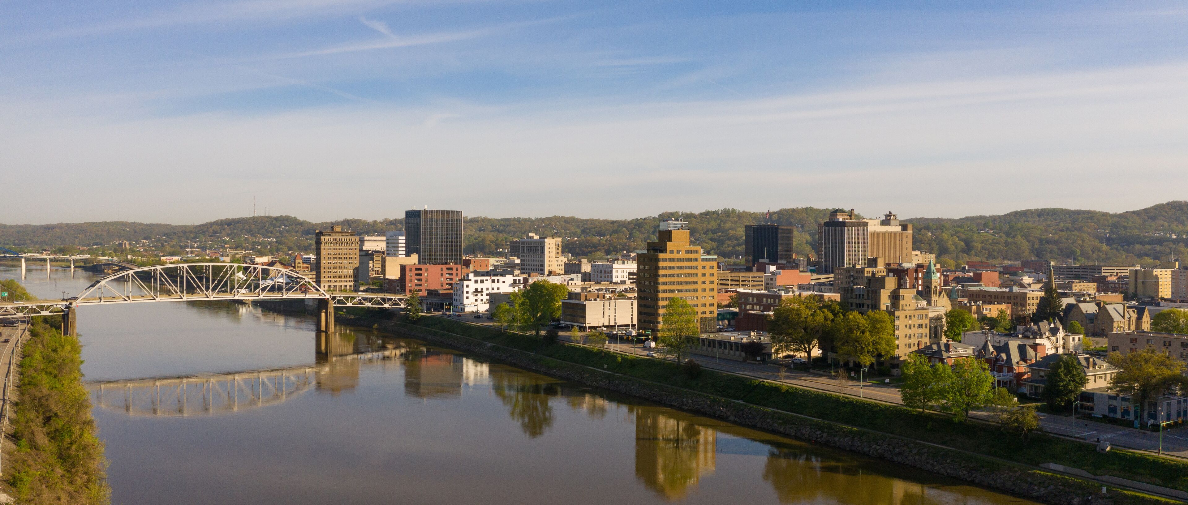 A river with a bridge, a cityscape with various buildings, and hills in the background.