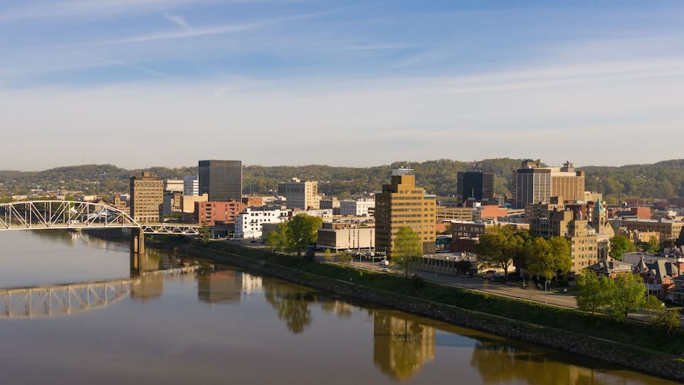 A river with a bridge, a cityscape with various buildings, and hills in the background.