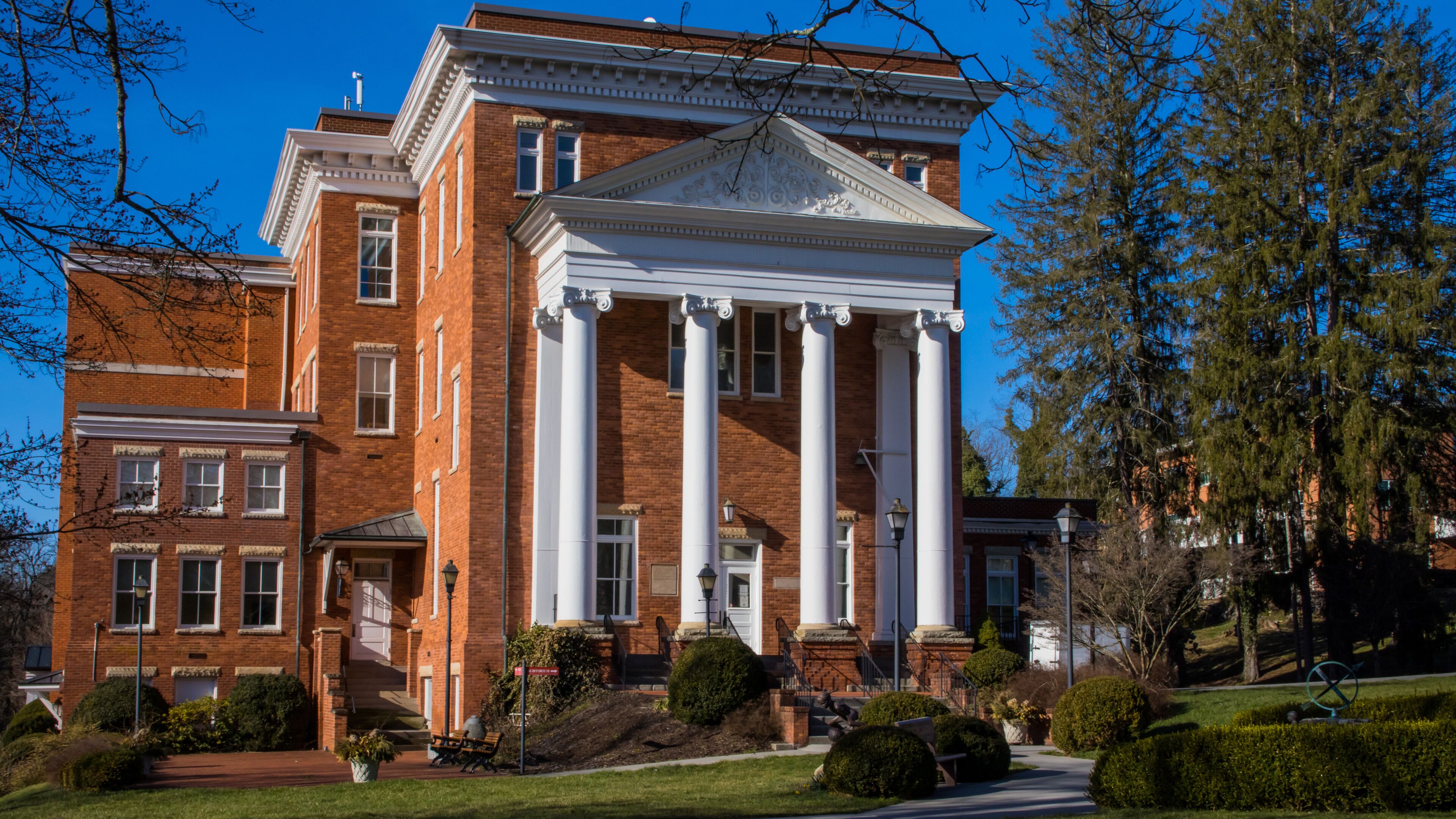 A large brick building with a central portico and columns, surrounded by well-maintained lawns and trees.