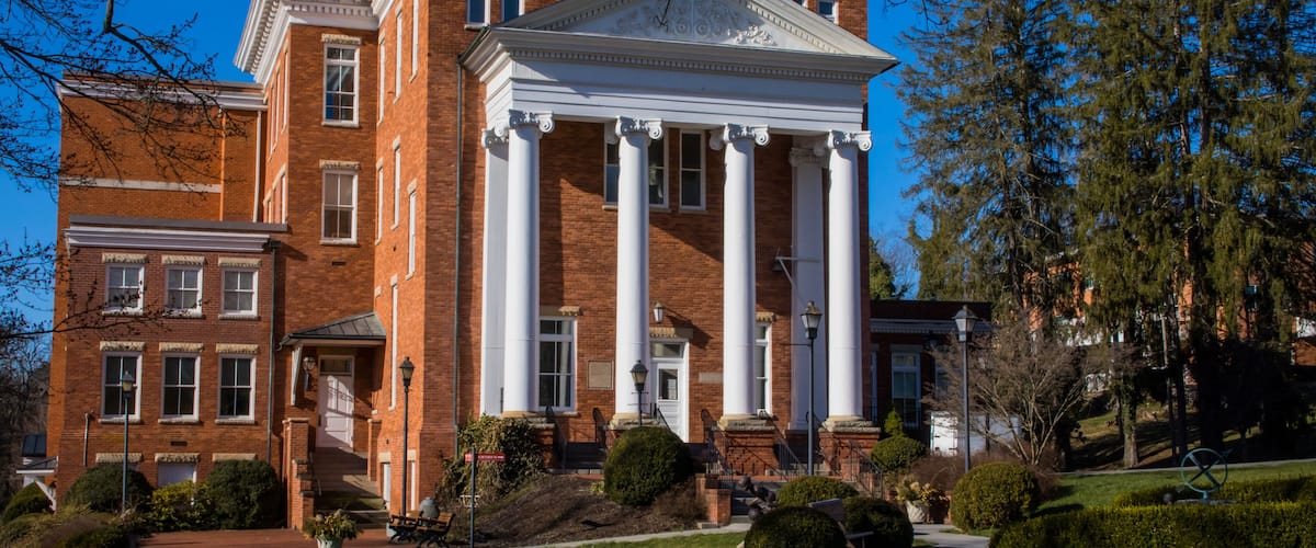 A large brick building with a central portico and columns, surrounded by well-maintained lawns and trees.