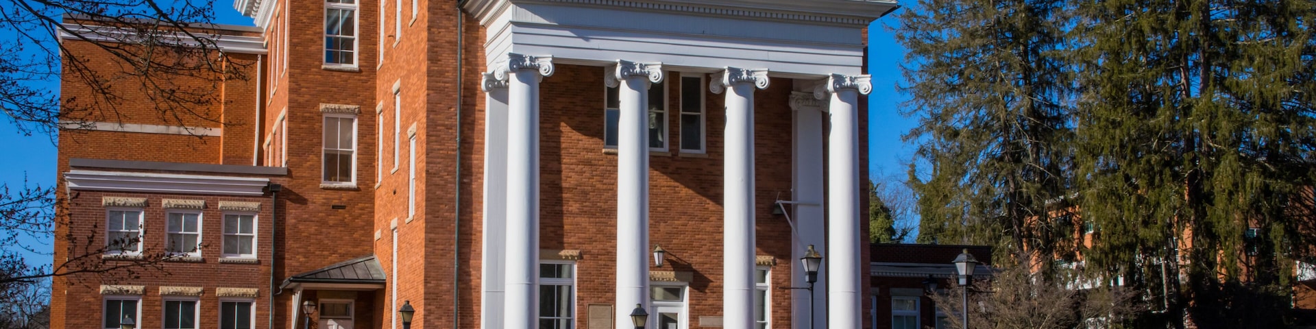 A large brick building with a central portico and columns, surrounded by well-maintained lawns and trees.