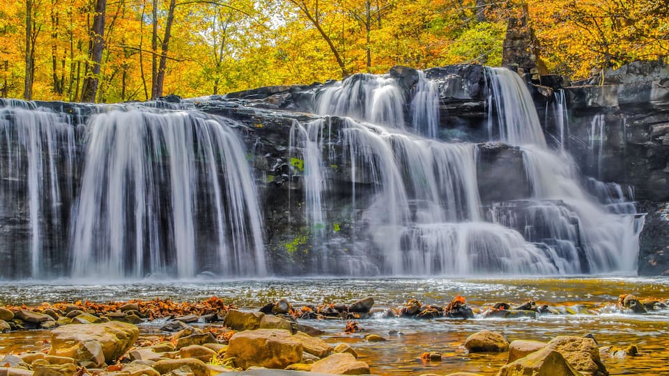 A waterfall cascading over rocks with autumn foliage in the background.