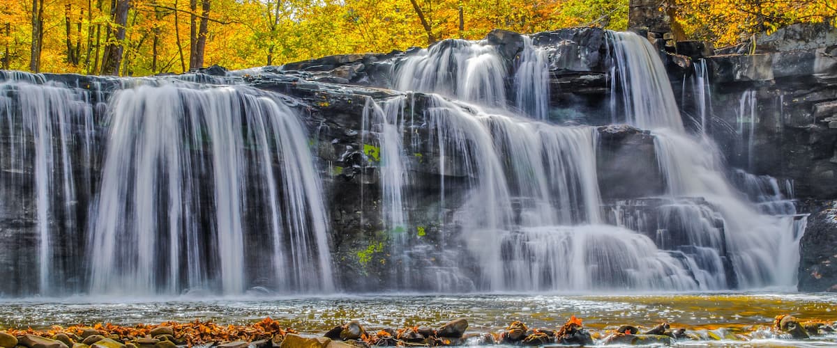 A waterfall cascading over rocks with autumn foliage in the background.