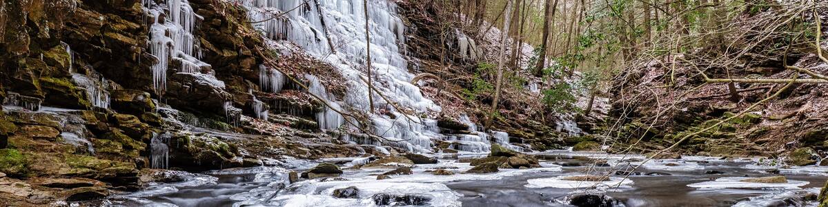 An icy mountain stream by a hiking trail with moss covered rocks and icicles hanging from bluff . The Fiery Gizzard creek on the Cumberland Plateau in Tracy City Tennessee USA.