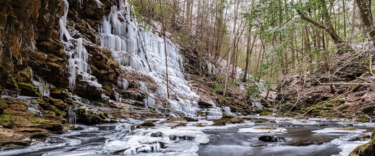 An icy mountain stream by a hiking trail with moss covered rocks and icicles hanging from bluff . The Fiery Gizzard creek on the Cumberland Plateau in Tracy City Tennessee USA.