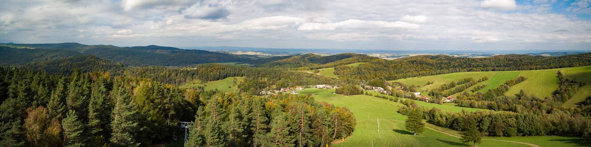 A mountainous landscape with a village nestled among rolling hills and dense forests.