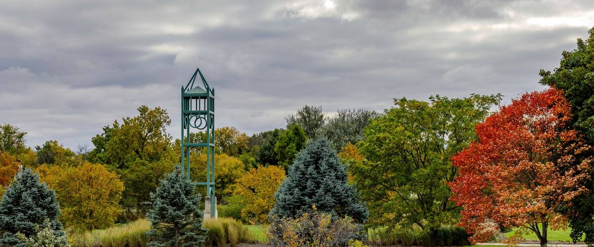 A park with a green gazebo, autumn-colored trees, and a cloudy sky.