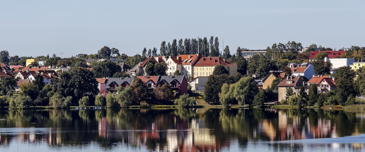 A lakeside town with red-roofed houses and trees reflecting on the water.