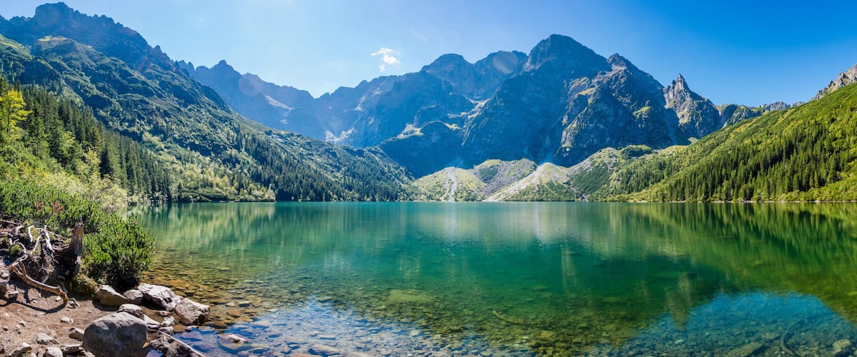 A mountain lake with clear water, surrounded by forested mountains.