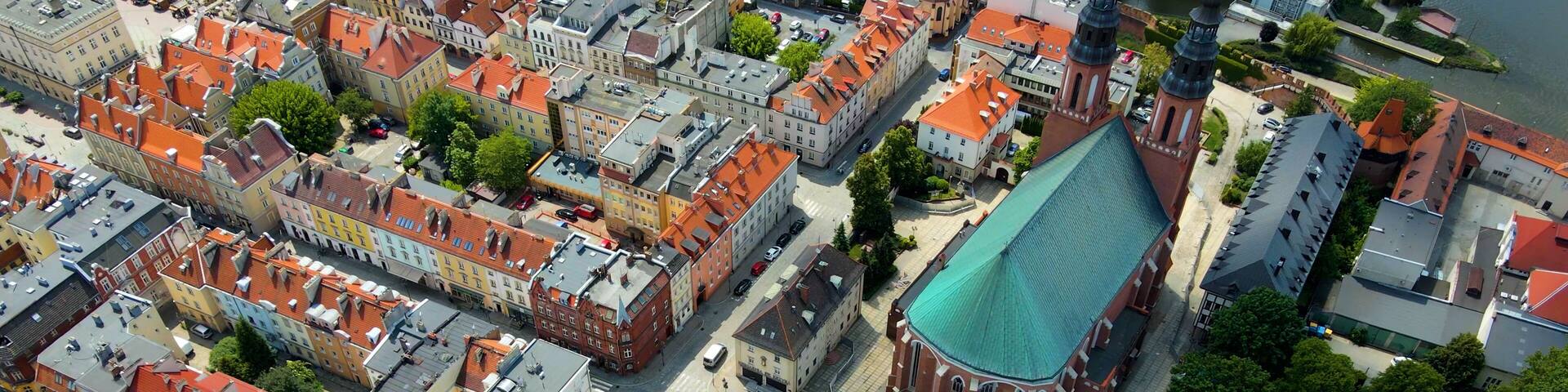 An aerial view of a historic European town with red-roofed buildings, a prominent church with a green roof, and a river in the background.