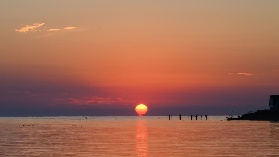 A sunset over a calm sea with a pier extending into the water.