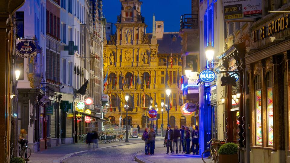 Una calle europea histórica iluminada de noche, con edificios brillantes y gente caminando.
