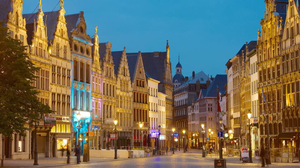 A historic European street at dusk with ornate buildings and illuminated signs.