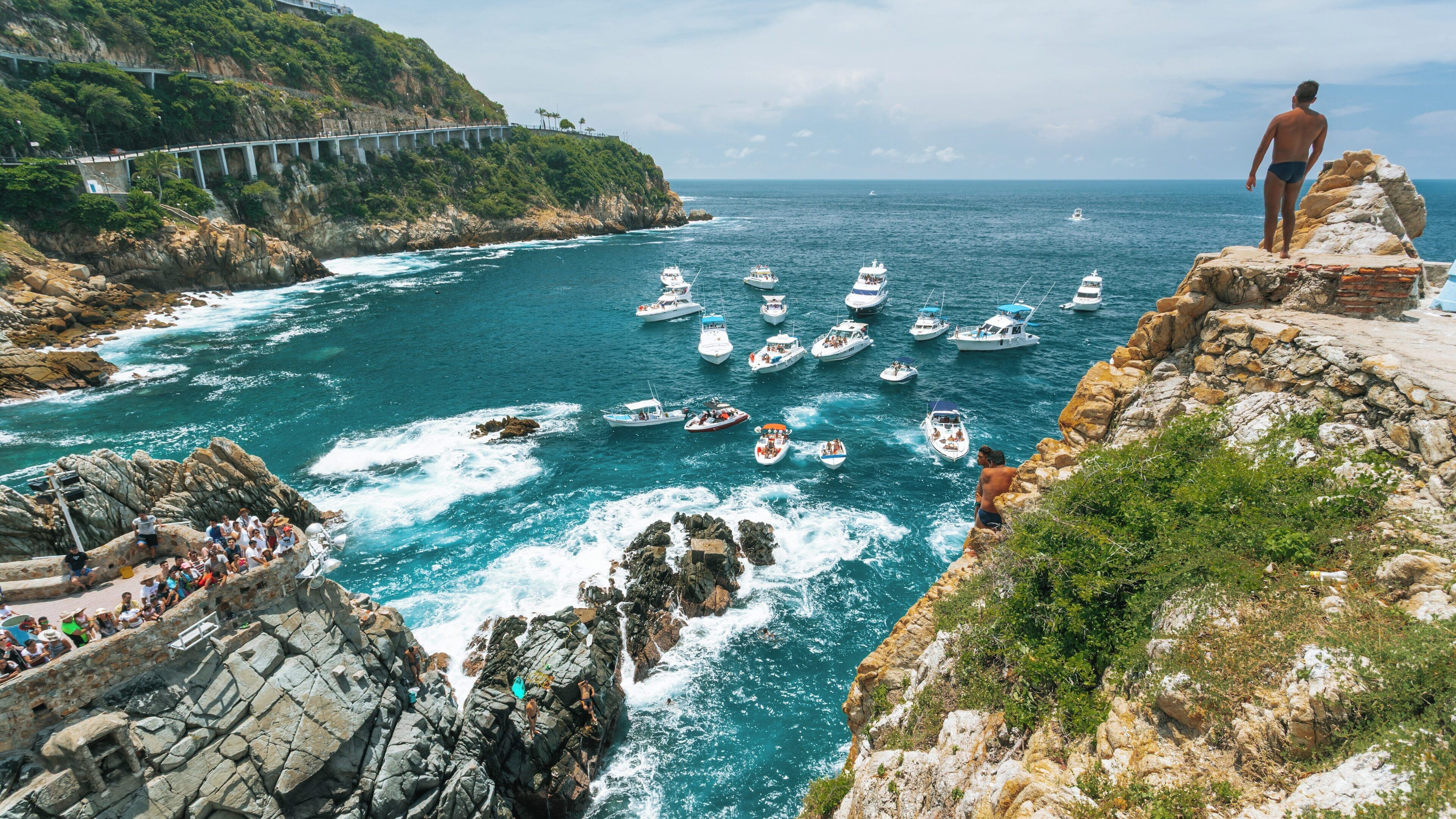 Scenic view of La Quebrada Cliffs with divers and boats in Acapulco, Guerrero featuring beautiful coastal waters