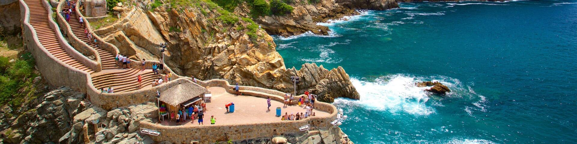 A coastal area with a stone staircase leading down to a beach, a bridge, and a cliff with greenery.