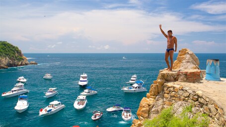 Ein Mann auf einer Klippe mit Blick aufs Meer und mehreren Booten.