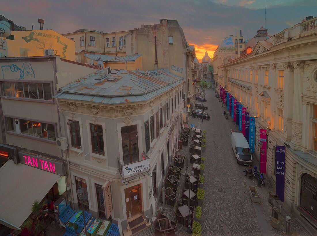 Una calle empedrada bordeada de edificios, un bar llamado 'Tan Tan' y un atardecer al fondo.