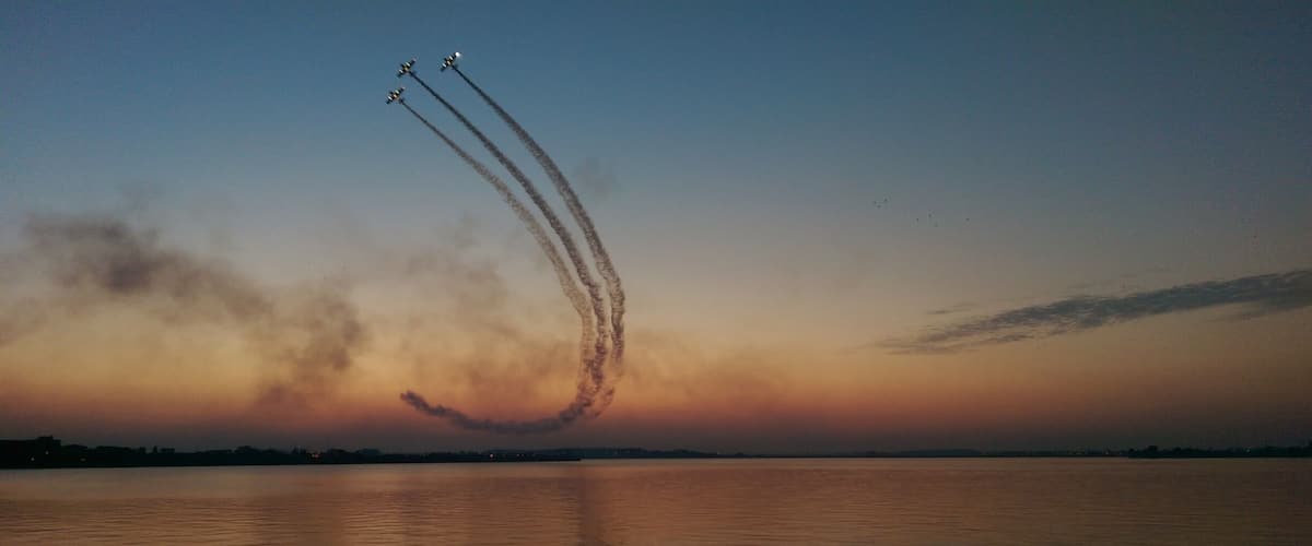 A sunset over a body of water with aircraft performing an aerial maneuver.