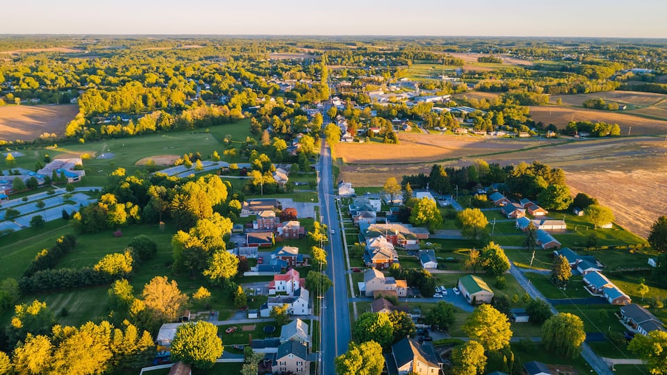 An aerial view of a suburban area with houses, roads, and green fields.