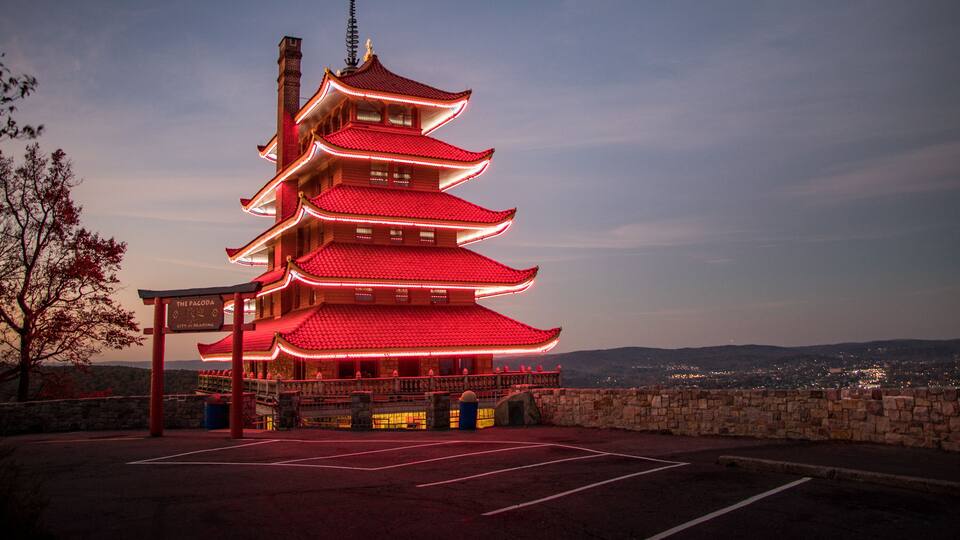 A traditional Japanese pagoda with multiple tiers, illuminated by red lights, set against a twilight sky.