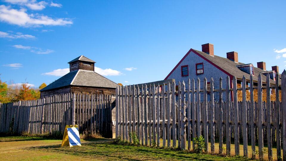 A wooden fence, a small building, and a larger house with a red roof.