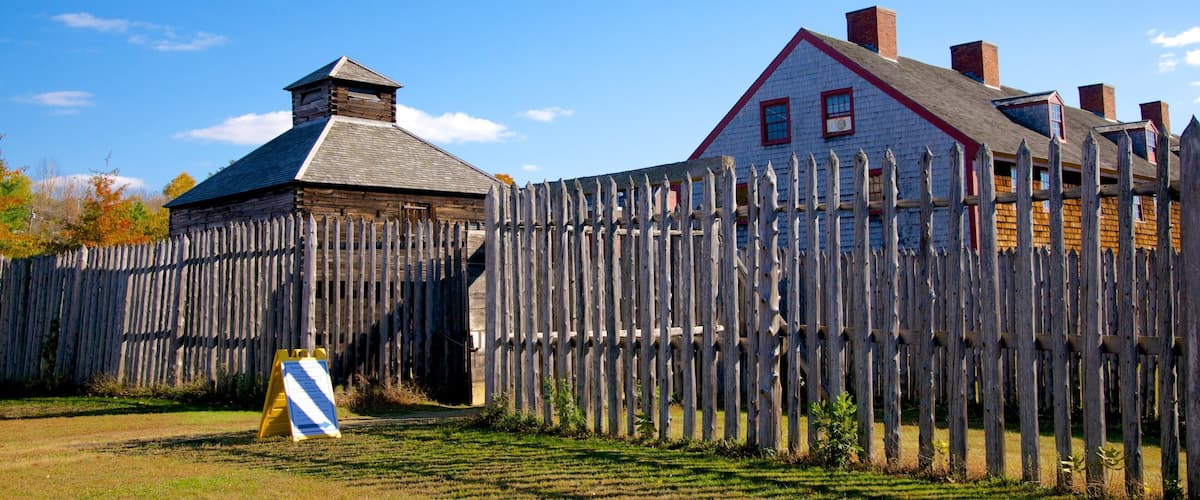 A wooden fence, a small building, and a larger house with a red roof.